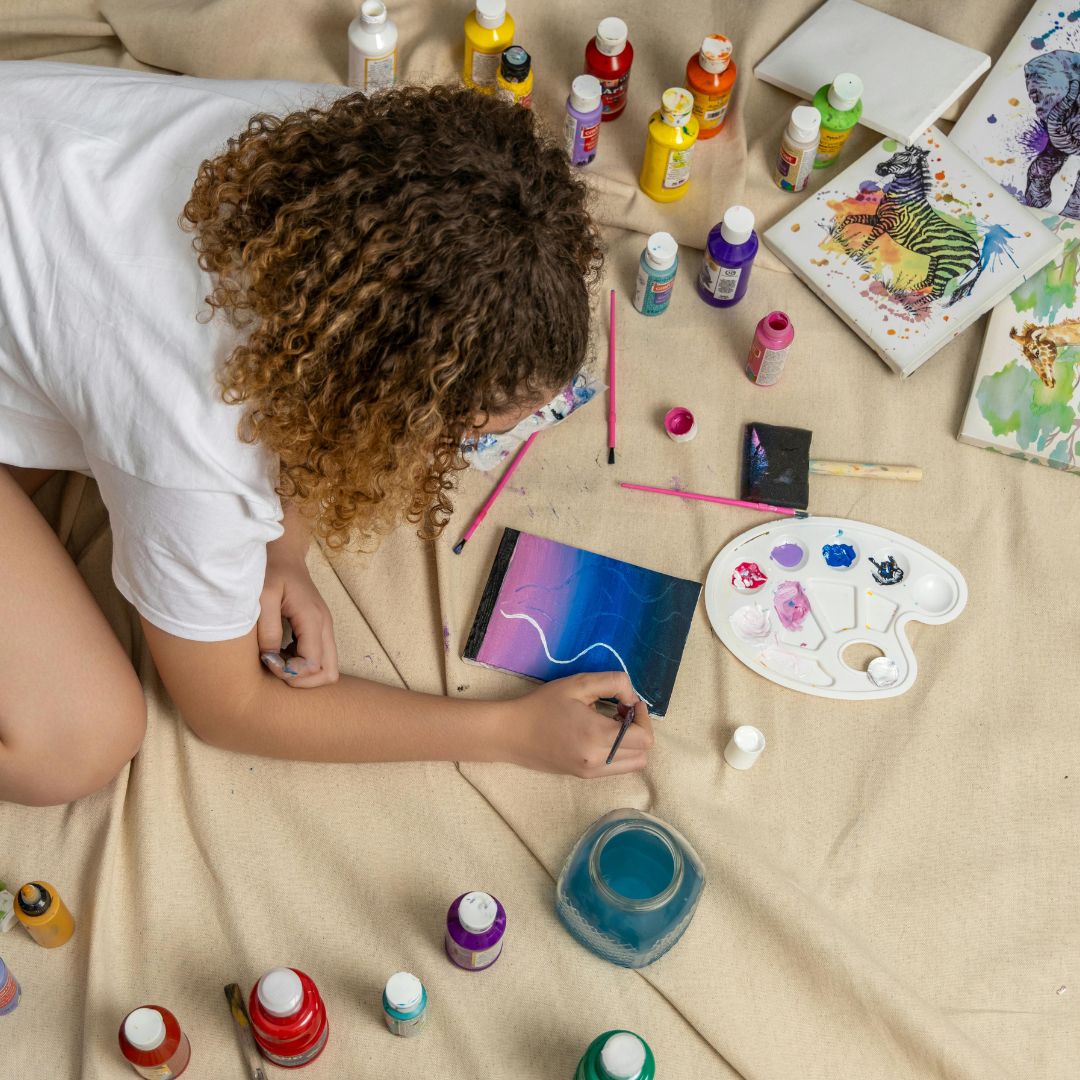 Person painting on a blanket with art supplies around